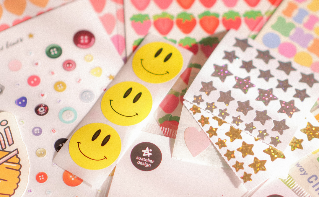 Collection of colorful sticker sheets with various designs including smiley faces, hearts, and stars.